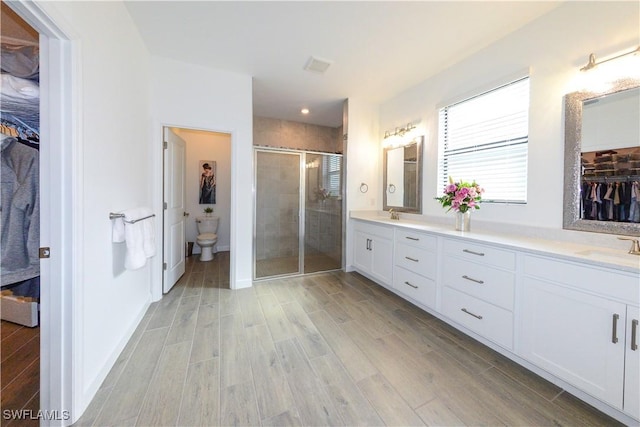 full bath featuring a stall shower, toilet, double vanity, wood finished floors, and a spacious closet