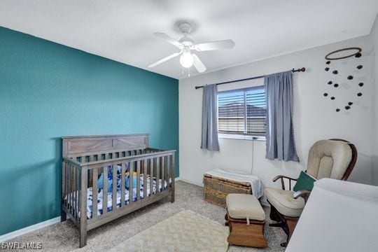 bedroom with a crib, light carpet, and ceiling fan