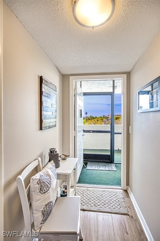 doorway featuring wood finished floors, baseboards, and a textured ceiling