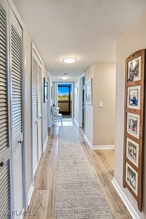 hall featuring light wood-type flooring, baseboards, and a textured ceiling