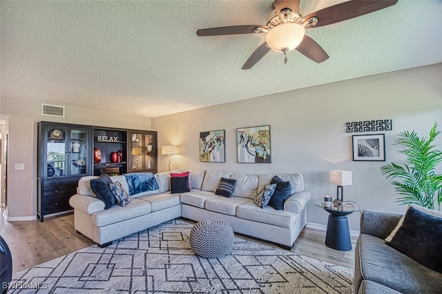 living area featuring a ceiling fan, wood finished floors, visible vents, and a textured ceiling