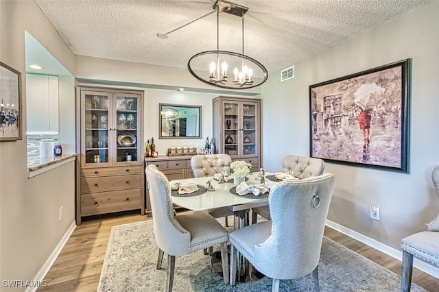 dining space featuring visible vents, baseboards, light wood-style flooring, a notable chandelier, and a textured ceiling