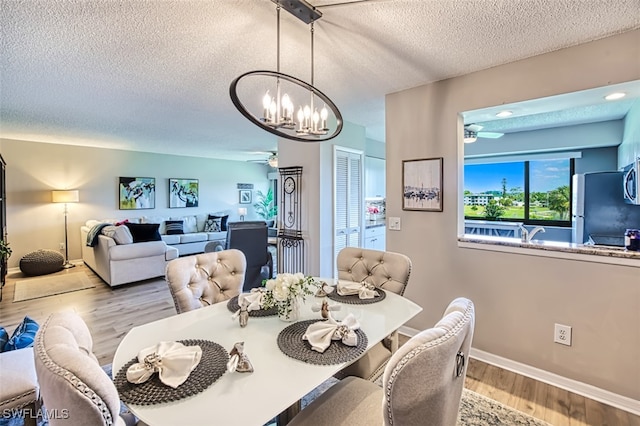 dining space featuring wood finished floors, ceiling fan with notable chandelier, baseboards, and a textured ceiling