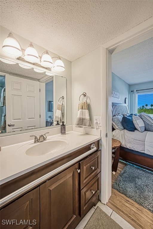 ensuite bathroom with connected bathroom, a textured ceiling, wood finished floors, and vanity