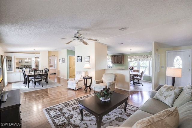 living room with ceiling fan with notable chandelier, light hardwood / wood-style flooring, and a textured ceiling