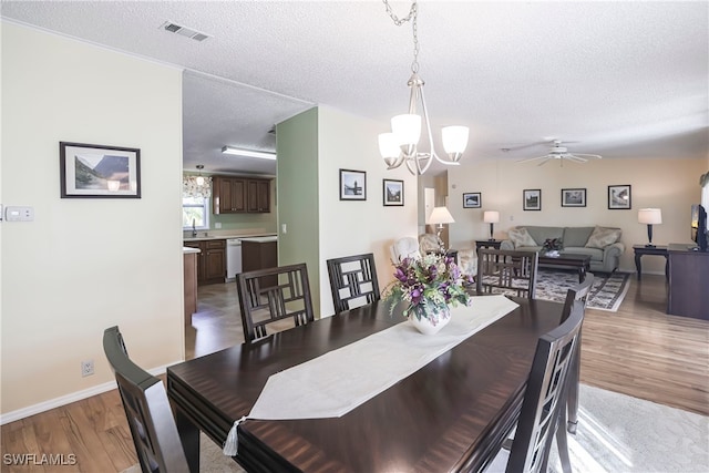 dining space with sink, ceiling fan with notable chandelier, light hardwood / wood-style flooring, and a textured ceiling