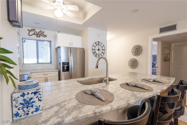 kitchen featuring a sink, visible vents, light stone countertops, stainless steel fridge, and a kitchen bar