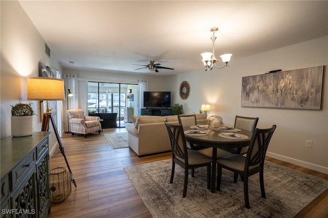 dining space with ceiling fan with notable chandelier, visible vents, baseboards, and wood finished floors