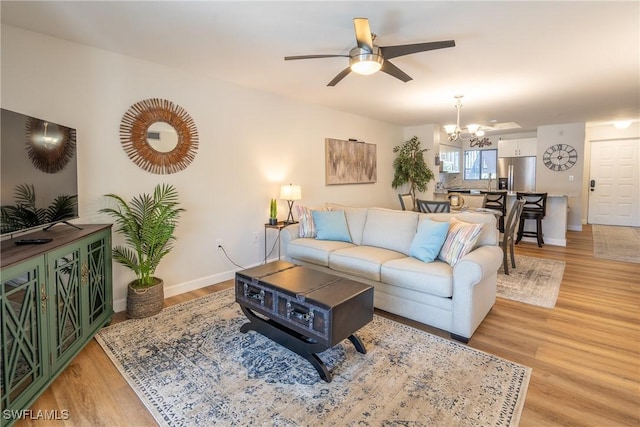 living room featuring baseboards, light wood finished floors, and ceiling fan with notable chandelier