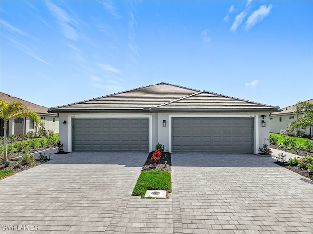 view of front of house featuring stucco siding, a tiled roof, decorative driveway, and a garage