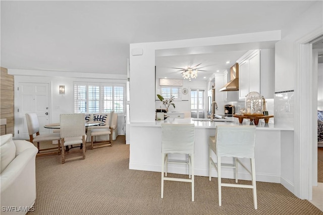 kitchen with white cabinetry, kitchen peninsula, sink, a kitchen bar, and wall chimney exhaust hood