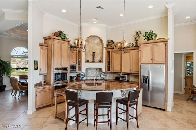 kitchen featuring appliances with stainless steel finishes, dark stone counters, decorative light fixtures, a breakfast bar, and a kitchen island with sink