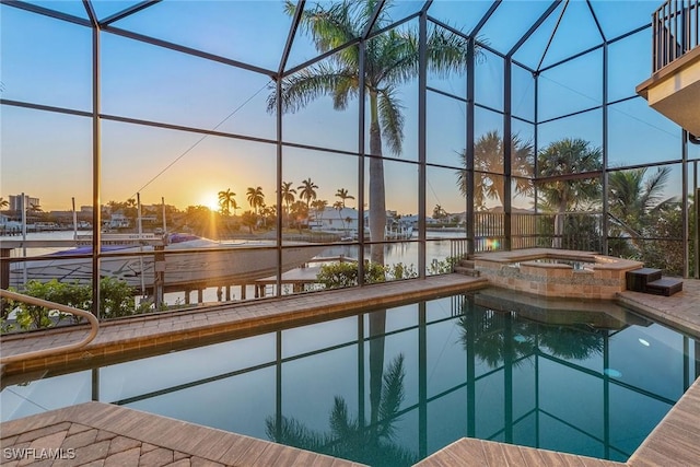 pool at dusk with an in ground hot tub, a water view, and a lanai