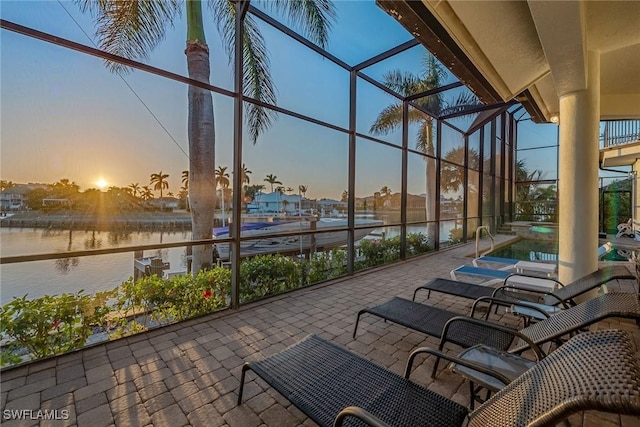 patio terrace at dusk featuring a water view and glass enclosure