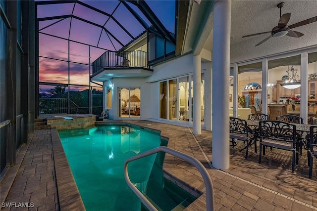 pool at dusk with an in ground hot tub, glass enclosure, a patio area, and ceiling fan