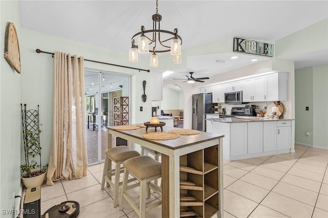 kitchen featuring arched walkways, light tile patterned floors, a peninsula, white cabinets, and appliances with stainless steel finishes