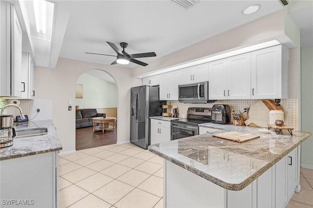 kitchen featuring arched walkways, light tile patterned floors, stainless steel appliances, a sink, and a peninsula