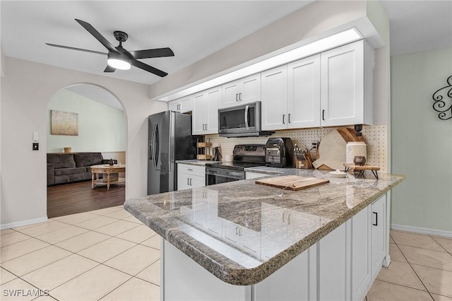 kitchen featuring appliances with stainless steel finishes, arched walkways, light tile patterned flooring, and backsplash