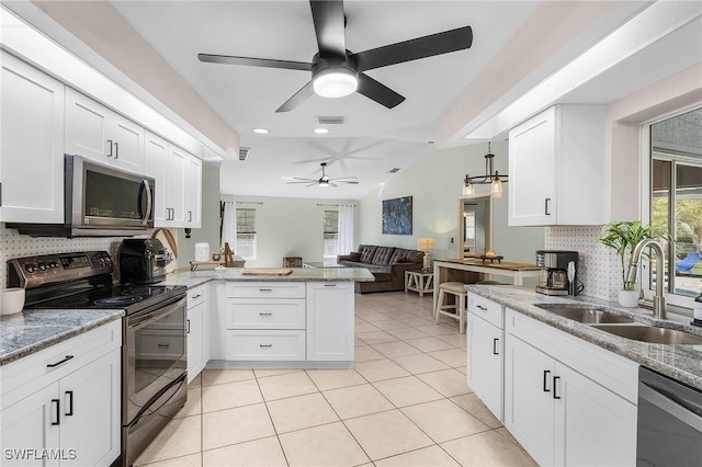 kitchen with light tile patterned flooring, a peninsula, a sink, white cabinetry, and appliances with stainless steel finishes