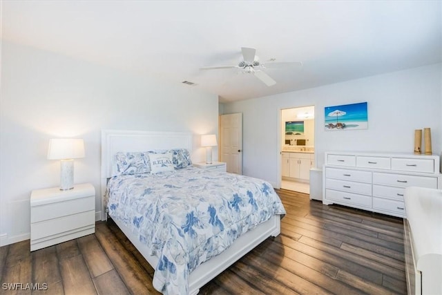 bedroom featuring dark wood finished floors, visible vents, ceiling fan, ensuite bath, and baseboards