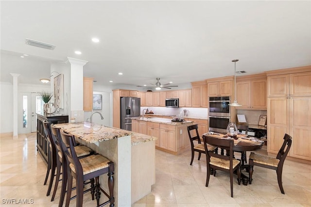 kitchen featuring visible vents, light brown cabinetry, stainless steel appliances, a breakfast bar area, and light stone countertops