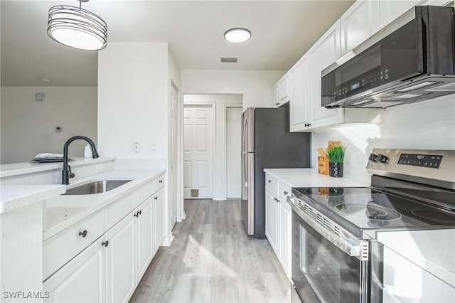 kitchen with sink, white cabinets, light stone counters, stainless steel appliances, and light hardwood / wood-style flooring