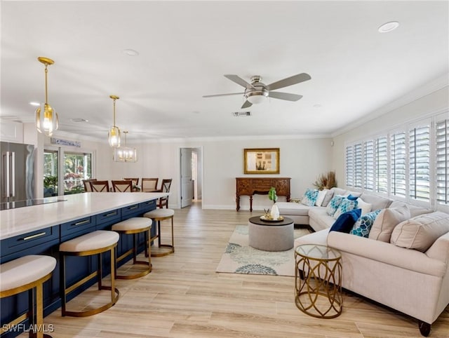 living room with light wood finished floors, visible vents, baseboards, a ceiling fan, and crown molding