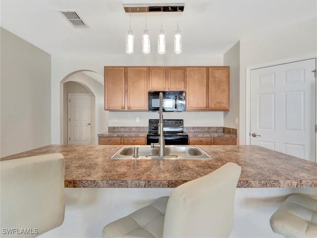 kitchen with sink, decorative light fixtures, a kitchen breakfast bar, an island with sink, and black appliances