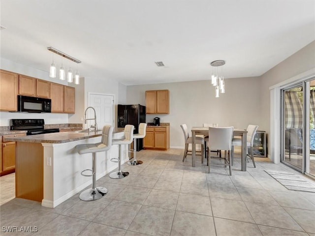 kitchen with hanging light fixtures, black appliances, sink, and a center island with sink