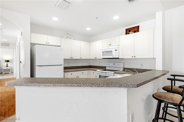 kitchen with a breakfast bar area, white cabinets, white appliances, and kitchen peninsula