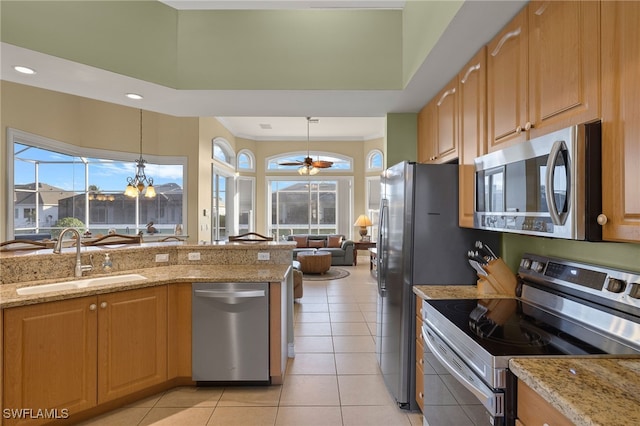 kitchen with sink, appliances with stainless steel finishes, light stone counters, a healthy amount of sunlight, and decorative light fixtures