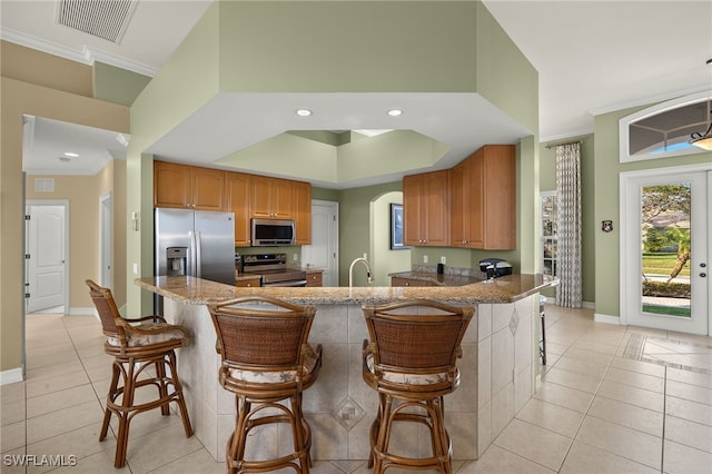 kitchen with crown molding, appliances with stainless steel finishes, kitchen peninsula, and a breakfast bar area