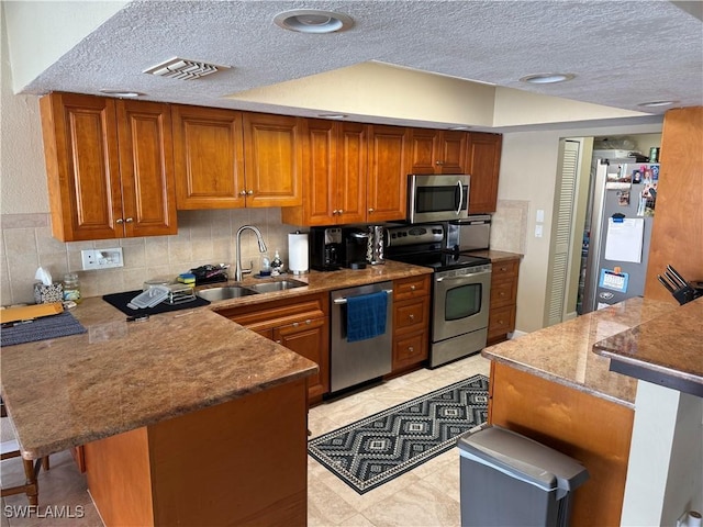 kitchen featuring a peninsula, a sink, appliances with stainless steel finishes, brown cabinets, and a kitchen bar