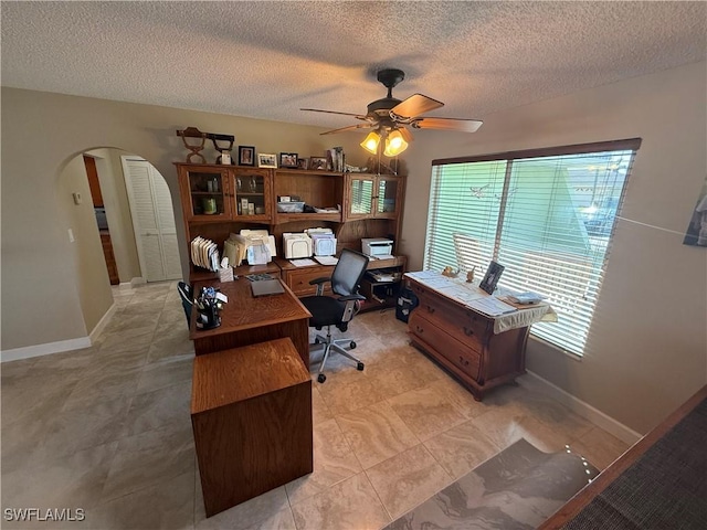 office featuring baseboards, a textured ceiling, arched walkways, and a ceiling fan