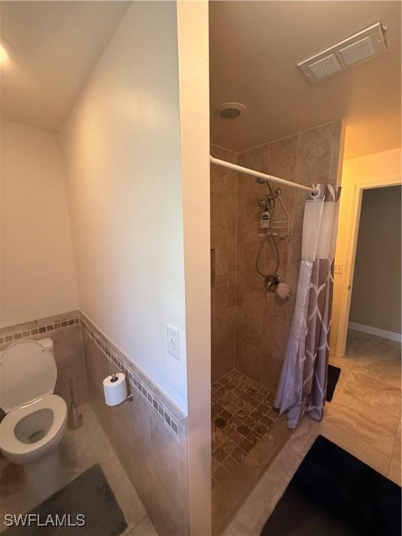 bathroom featuring toilet, visible vents, tile walls, tile patterned floors, and a stall shower