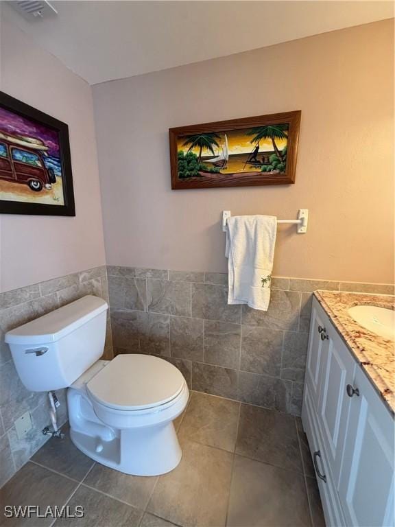 half bath featuring tile patterned flooring, toilet, visible vents, vanity, and tile walls