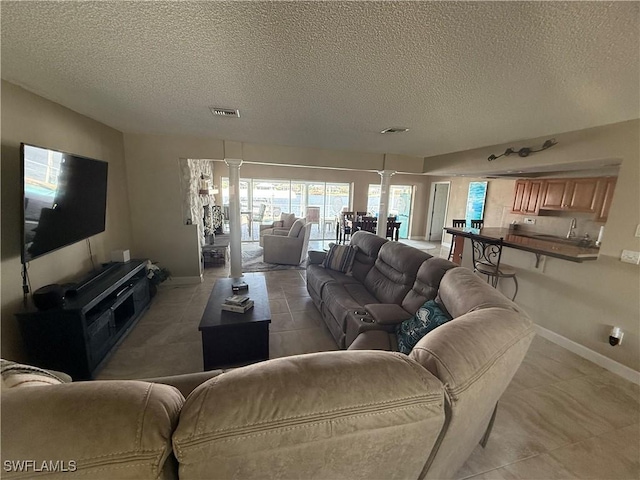 living area with decorative columns, a textured ceiling, visible vents, and baseboards