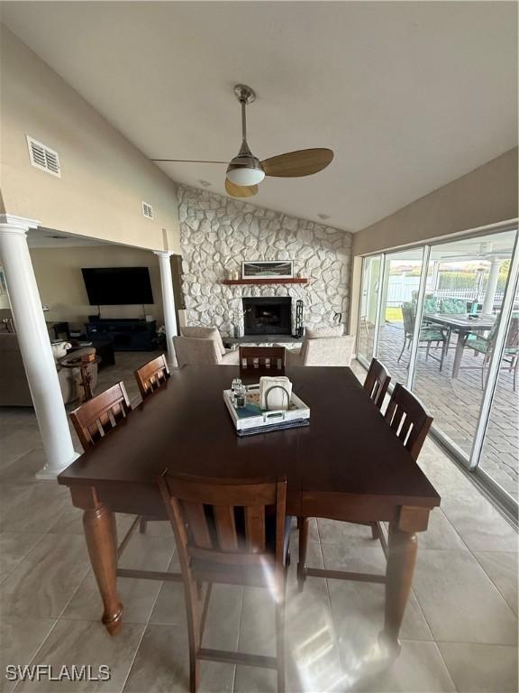tiled dining space with decorative columns, visible vents, a ceiling fan, lofted ceiling, and a fireplace