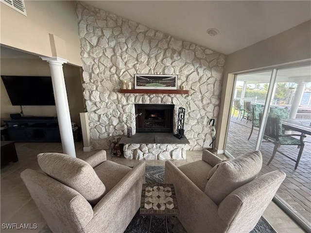 living area featuring high vaulted ceiling, a stone fireplace, visible vents, and ornate columns