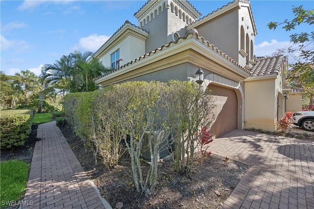 view of side of property with a garage, a tile roof, decorative driveway, and stucco siding