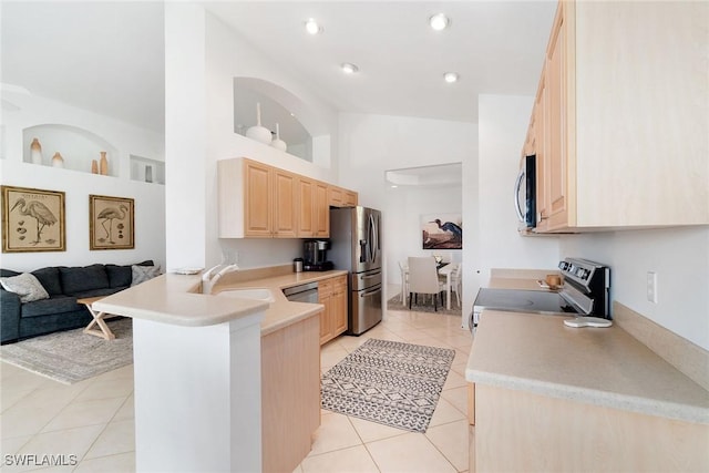 kitchen with light tile patterned floors, a peninsula, light brown cabinetry, appliances with stainless steel finishes, and a sink