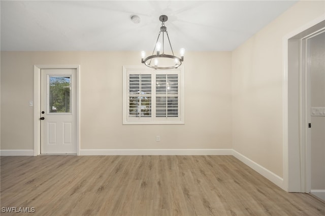 unfurnished dining area with a chandelier, baseboards, and light wood finished floors