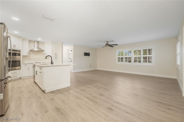 kitchen with a center island with sink, white cabinets, open floor plan, light countertops, and wall chimney range hood