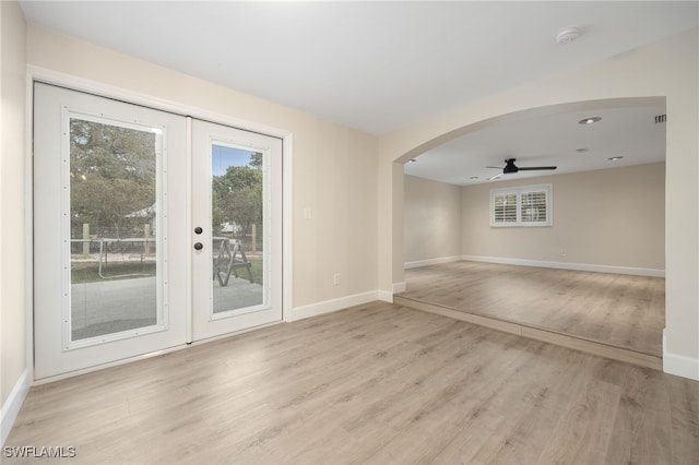 unfurnished room with light wood finished floors, baseboards, arched walkways, ceiling fan, and french doors