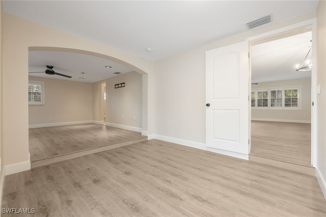 empty room featuring arched walkways, light wood finished floors, visible vents, ceiling fan, and baseboards