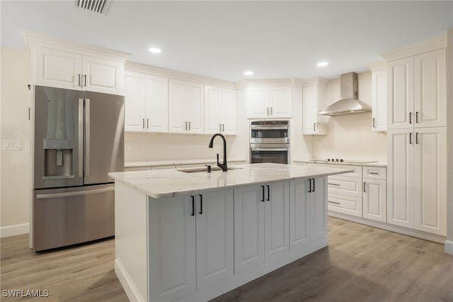 kitchen with an island with sink, wall chimney exhaust hood, appliances with stainless steel finishes, light stone countertops, and a sink