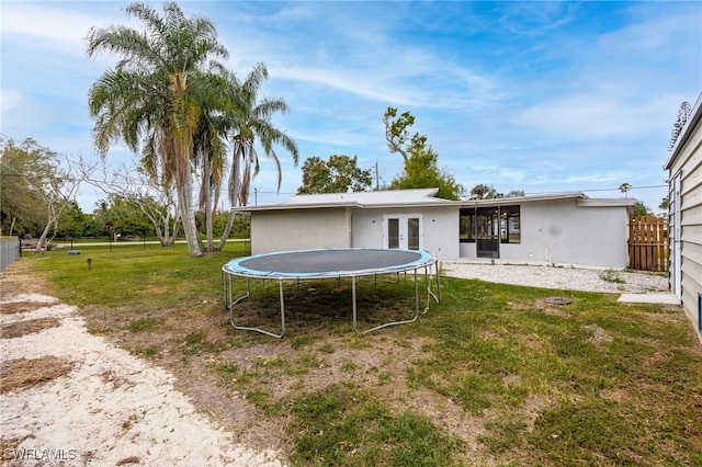rear view of property with stucco siding, a trampoline, fence, and a yard