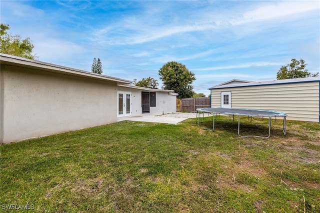 view of yard featuring a trampoline, fence, french doors, and a patio