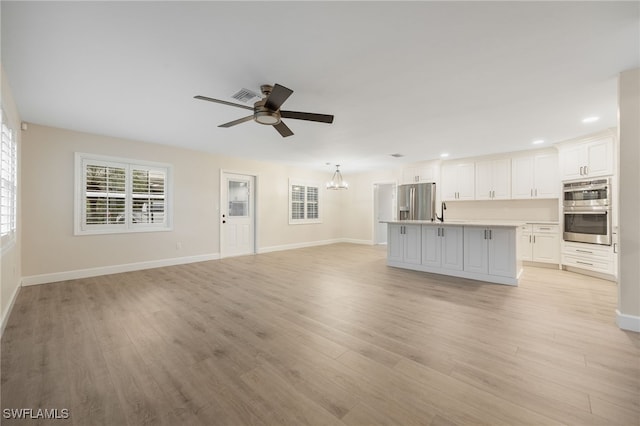 unfurnished living room with light wood-style floors, baseboards, visible vents, and ceiling fan with notable chandelier