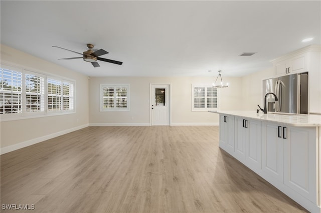 unfurnished living room featuring baseboards, visible vents, light wood finished floors, and ceiling fan with notable chandelier